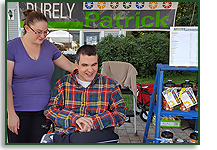 A blind man with intellectual disabilities sits beside his baking stand at a farmers market.