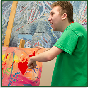 A young man with autism pointing to the heart on a painting he made.