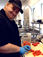 A chef cuts tomatos on a cutting board.